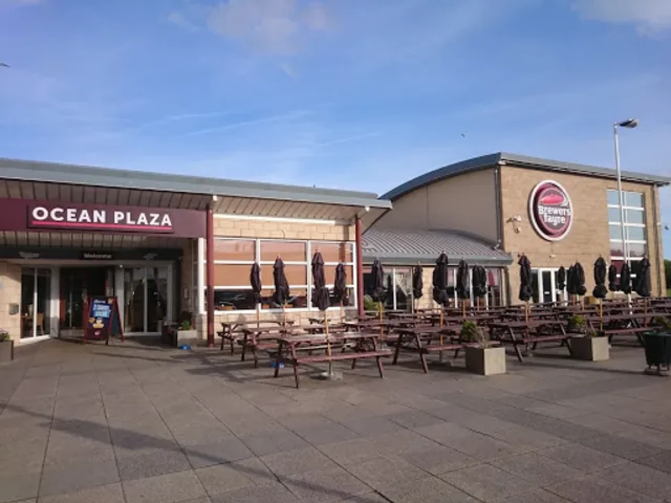 Ocean Plaza exterior with outdoor seating and Brewery's logo, clear blue sky