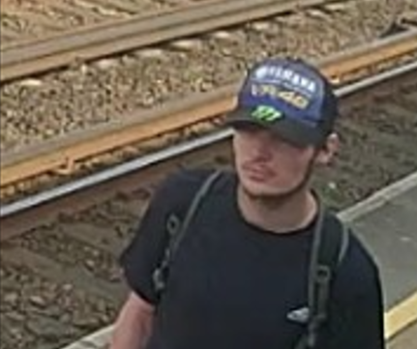 Young man wearing a cap and backpack standing near railway tracks