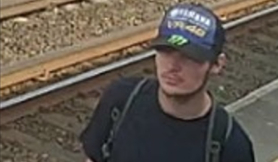 Young man wearing a cap and backpack standing near railway tracks