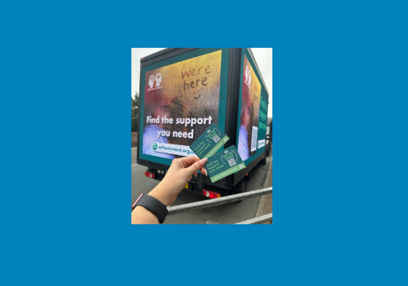 Person holding green informational cards in front of a blue advertisement truck.