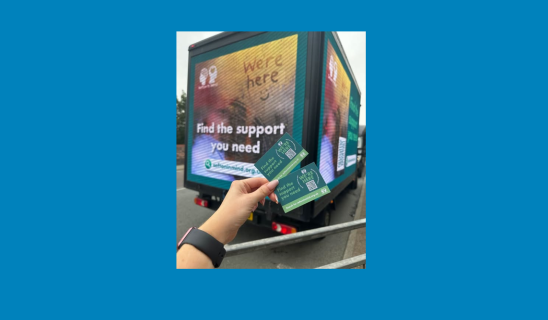 Person holding green informational cards in front of a blue advertisement truck.