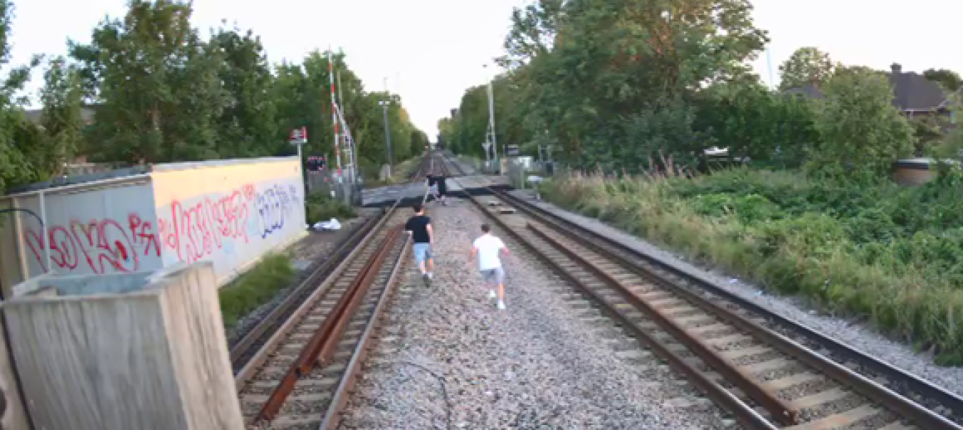 Two children running along a railway track toward a vanishing point with greenery and graffiti on walls nearby.