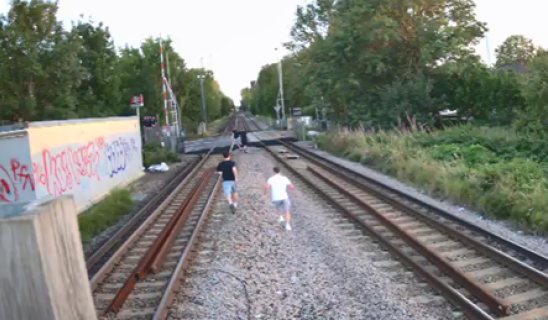 Two children running along a railway track toward a vanishing point with greenery and graffiti on walls nearby.