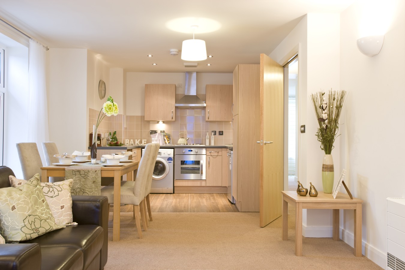 Bright open-plan kitchen and dining area with wooden cabinets, beige tiles, and dining table set for six.