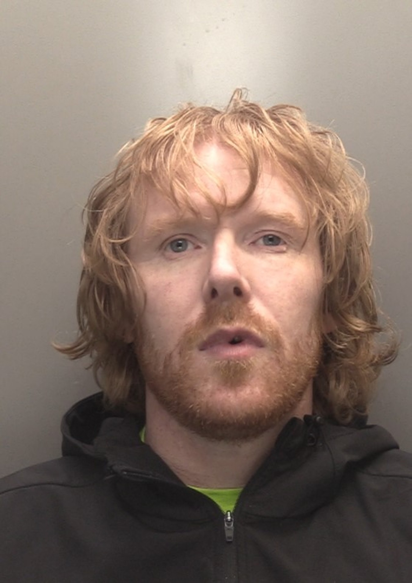 Man with shoulder-length light brown hair and stubble looking at camera.