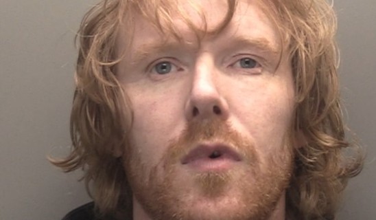 Man with shoulder-length light brown hair and stubble looking at camera.