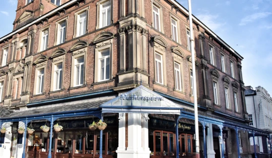 Terraced brick hotel building with blue awning on ground floor and hanging flower baskets