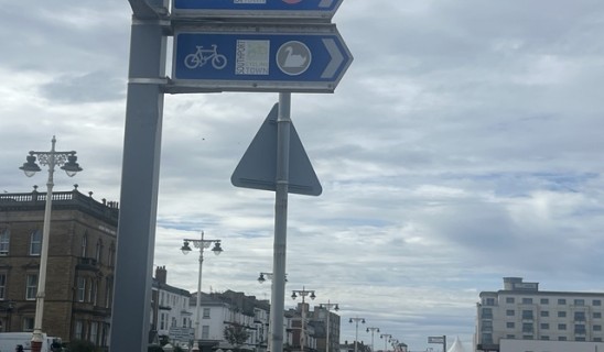 Signs directing cyclists and pedestrians along a seaside town street with historic buildings