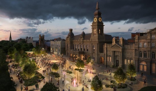 At dusk, a historic town hall with clock tower overlooks a lively public square with trees and a fountain.