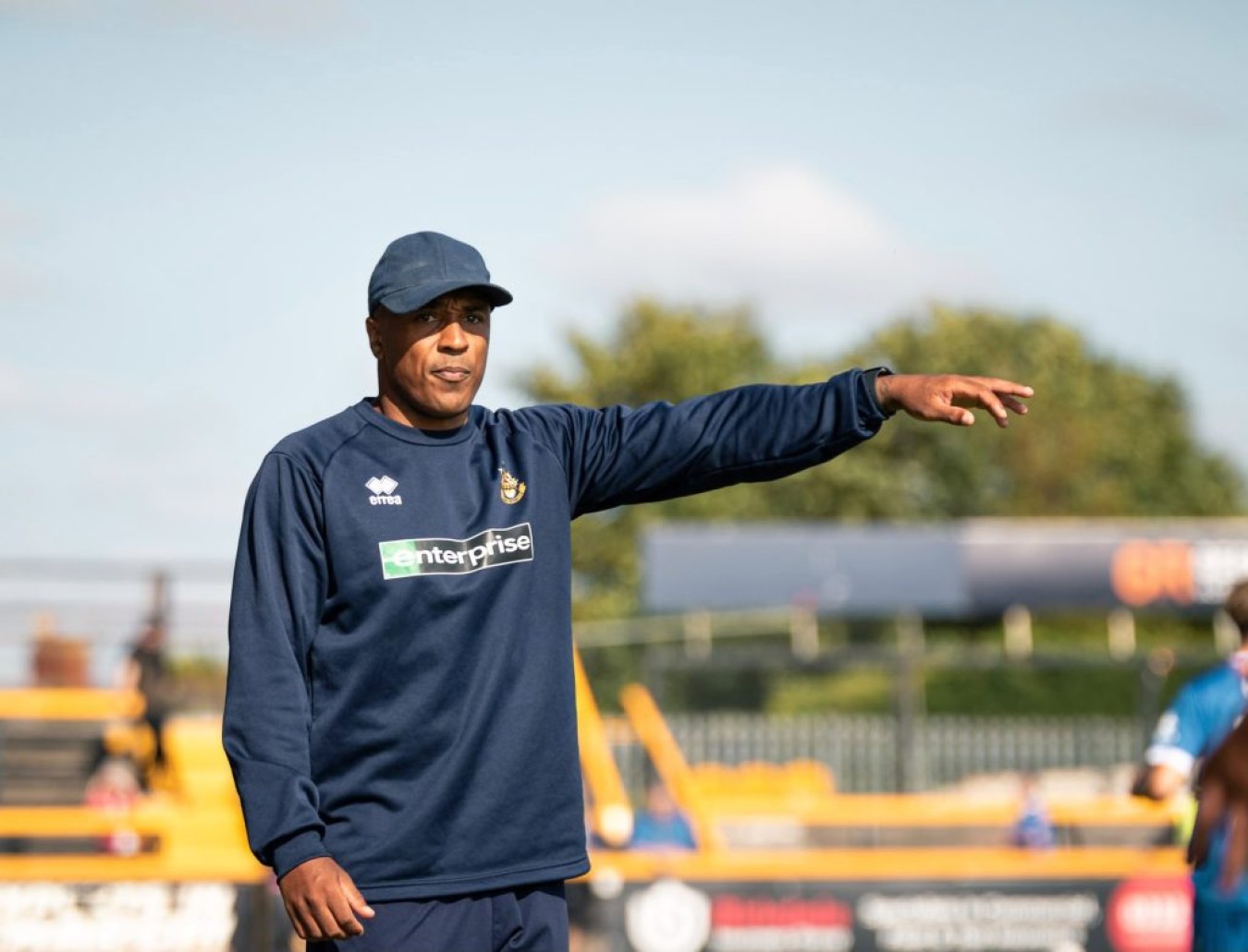 Athlete in navy sportswear points with outstretched arm on a sunny field.