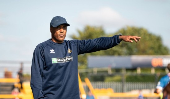 Athlete in navy sportswear points with outstretched arm on a sunny field.