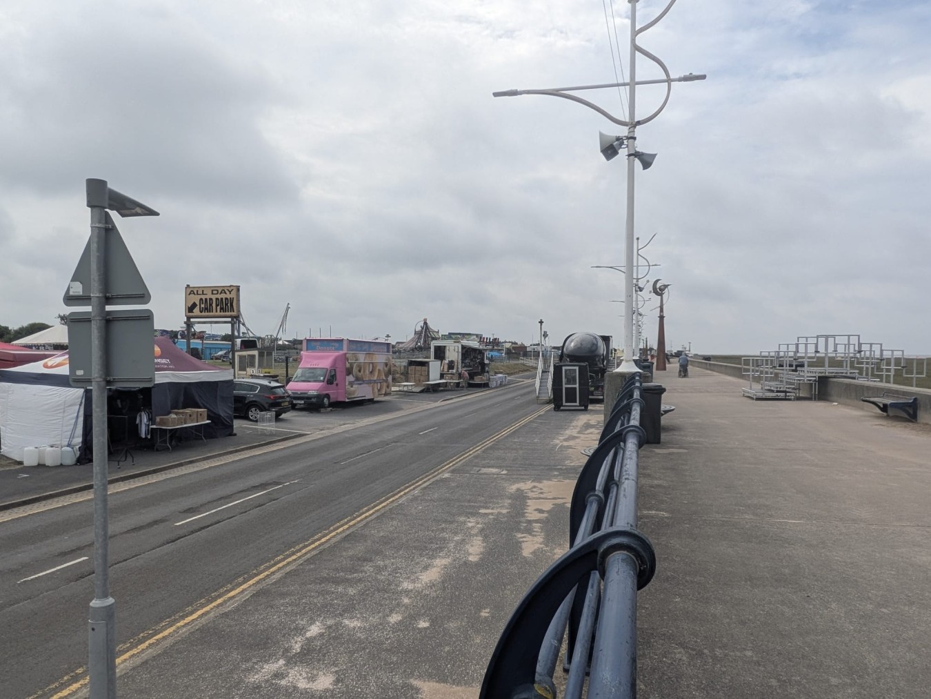 Seaside promenade with tents, signs and vendor stalls along a road.