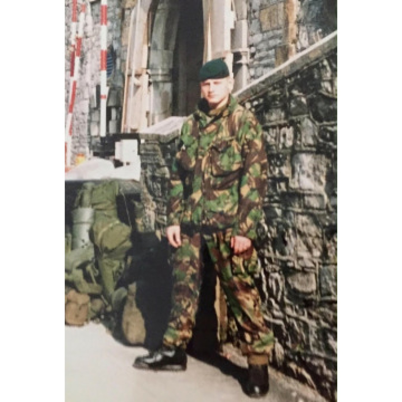 soldier in camouflage uniform standing beside stone wall in urban setting