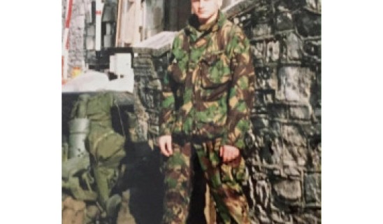 soldier in camouflage uniform standing beside stone wall in urban setting