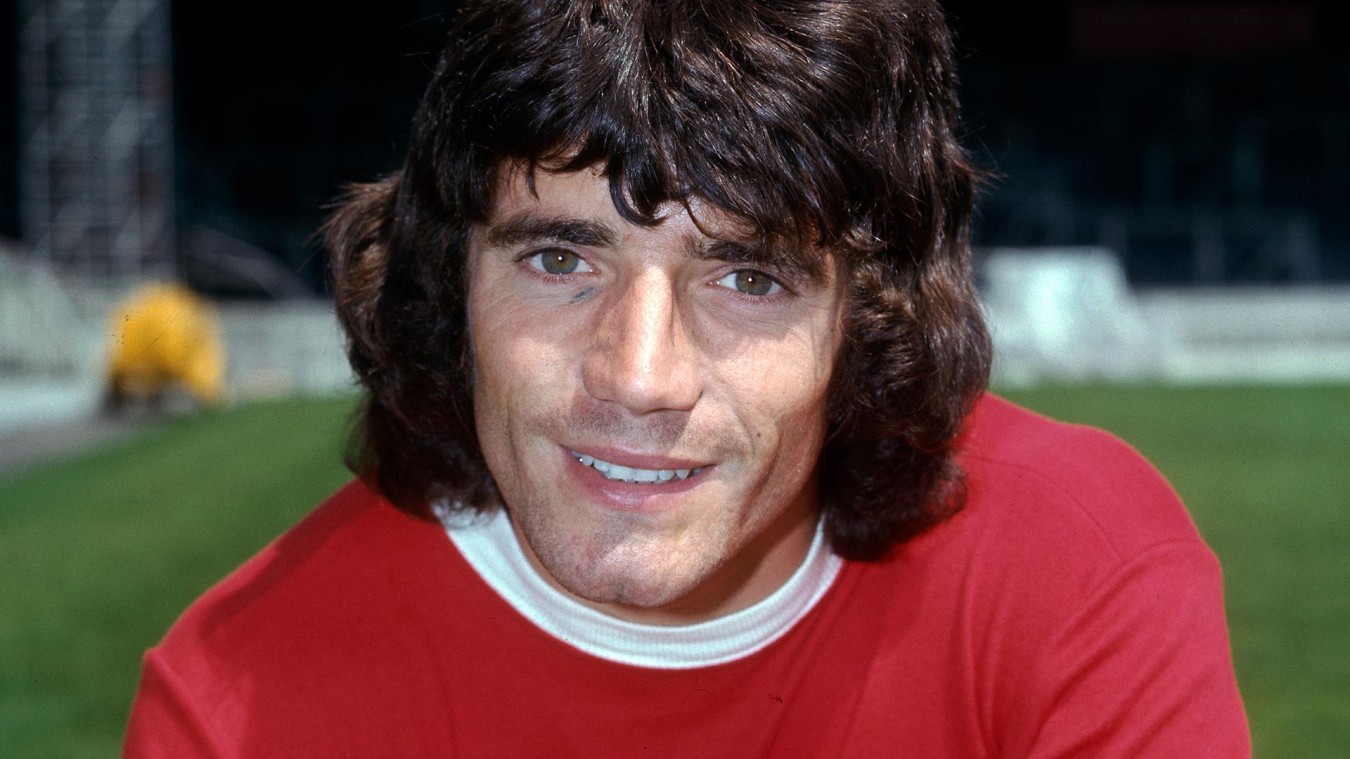 Man with dark hair smiling, wearing red shirt, outdoors at night.