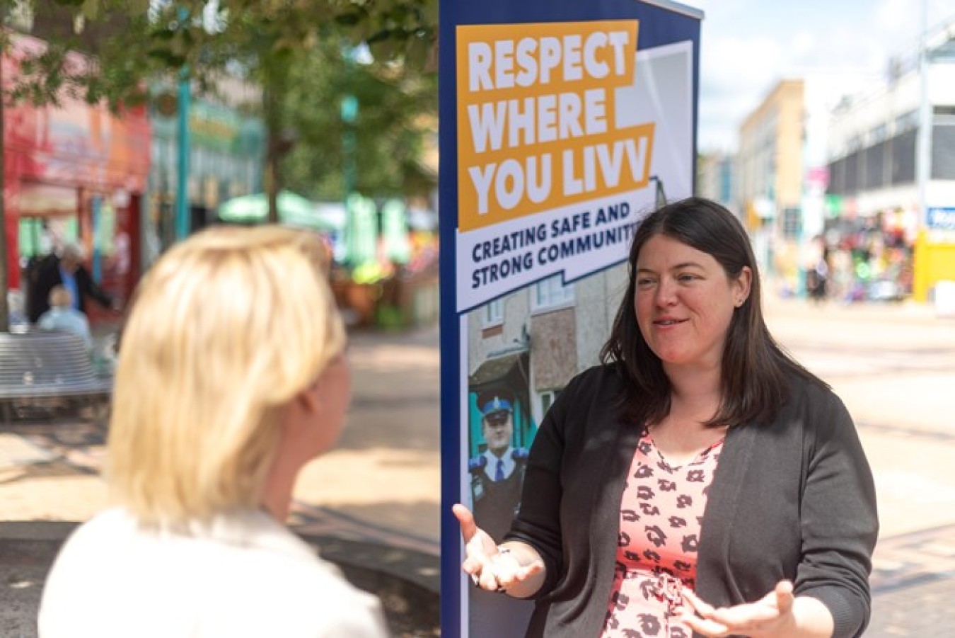 Two women talking on a sunny street, activist banner saying 'Respect Where You Lviv' in background.