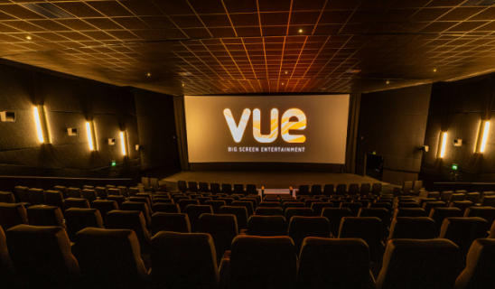 Empty cinema auditorium with large screen showing 'Vue' logo and seating rows in warm lighting