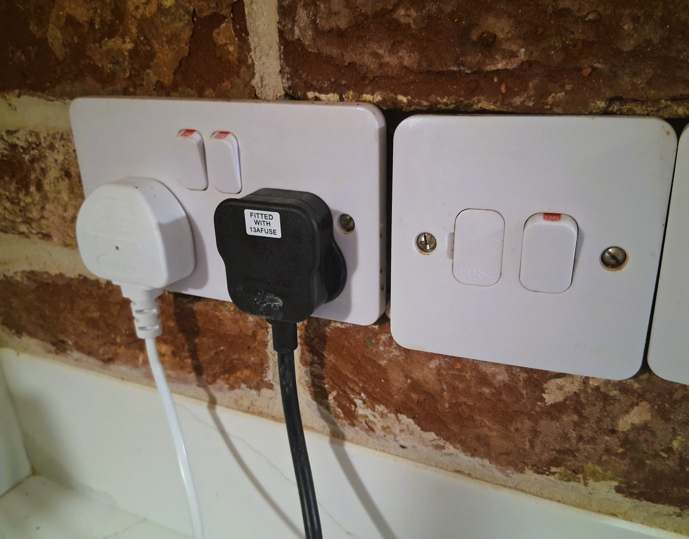 Close-up of a brown brick wall behind a double electrical socket plate with switches