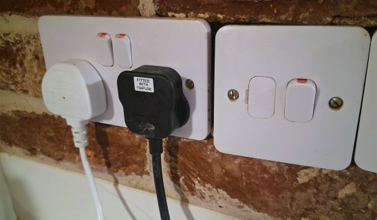 Close-up of a brown brick wall behind a double electrical socket plate with switches