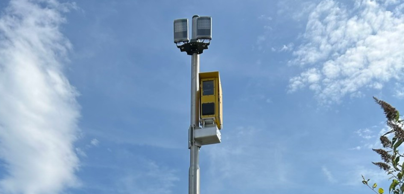 Traffic monitoring pole with camera and yellow device against a blue sky.