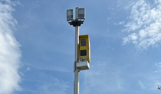Traffic monitoring pole with camera and yellow device against a blue sky.